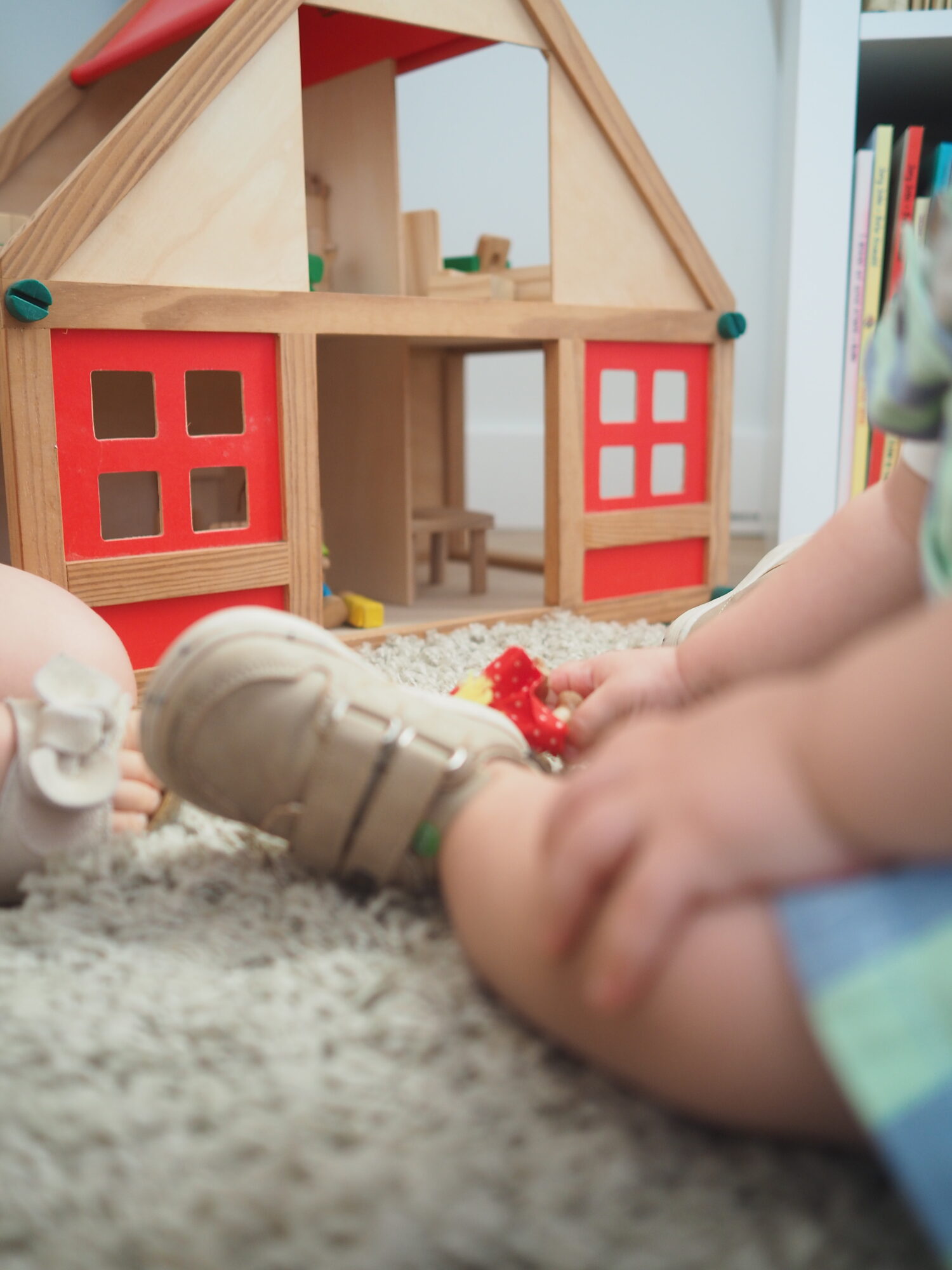 Bebé sentado no tapete a agarrar um brinquedo, junto a uma casa de madeira