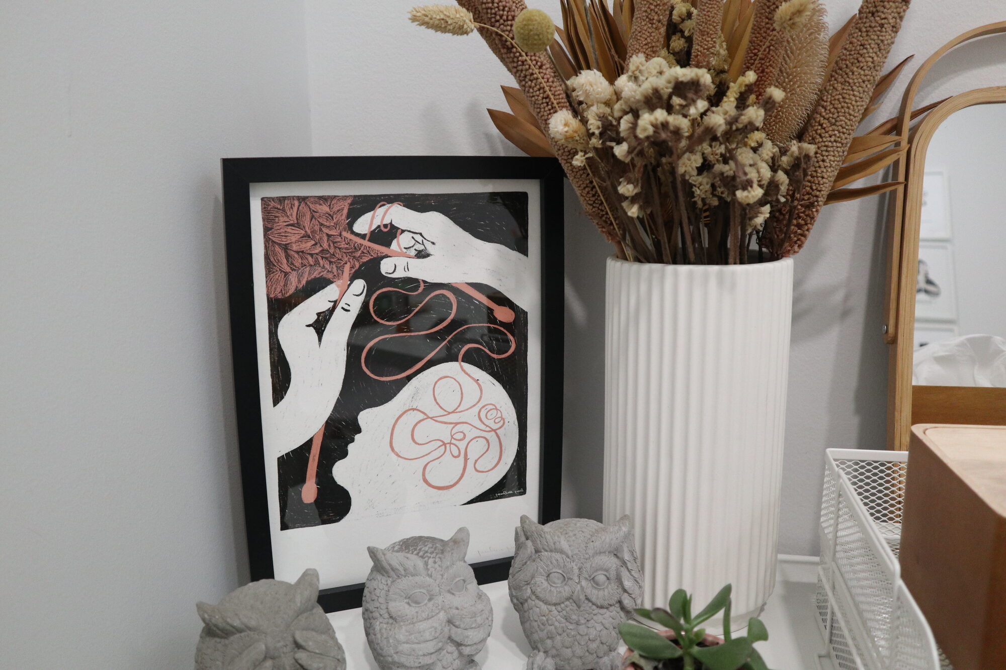 Quadro ilustrado, flores secas e corujas de pedra no espaço do Desenvolver+